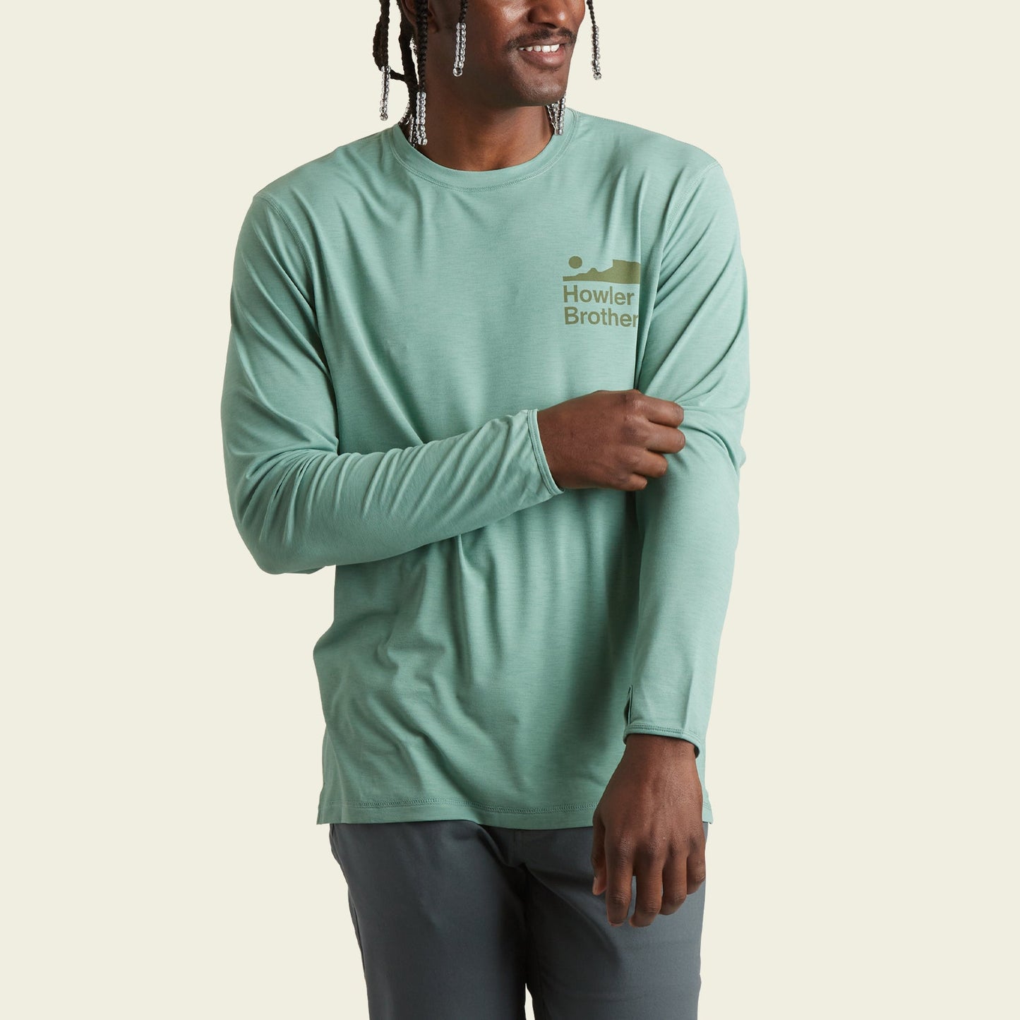 A person wearing a light green long-sleeve shirt with Howler Brothers and a small wave logo on the chest, perfect as a lightweight cover up offering UPF 50+ protection, stands against a plain light background. - View 3