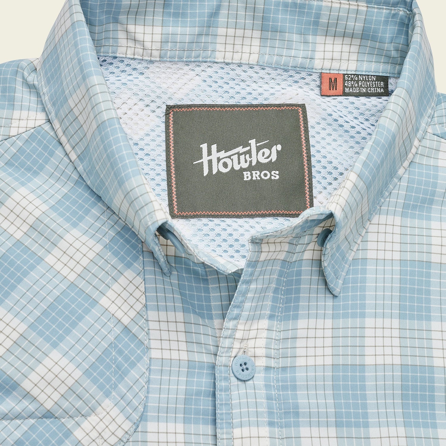 A light blue and white plaid Matagorda Shirt with a mesh inner lining, featuring a Howler Bros label and a size medium tag sewn inside the collar. This travel shirt is quick drying for comfort on the go. - View 7