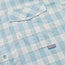 Close-up of a light blue and white checkered Matagorda Shirt with a buttoned chest pocket. The pocket features a blue button and a small fabric tag with the word Howler stitched in red. Ideal as a quick drying travel shirt.