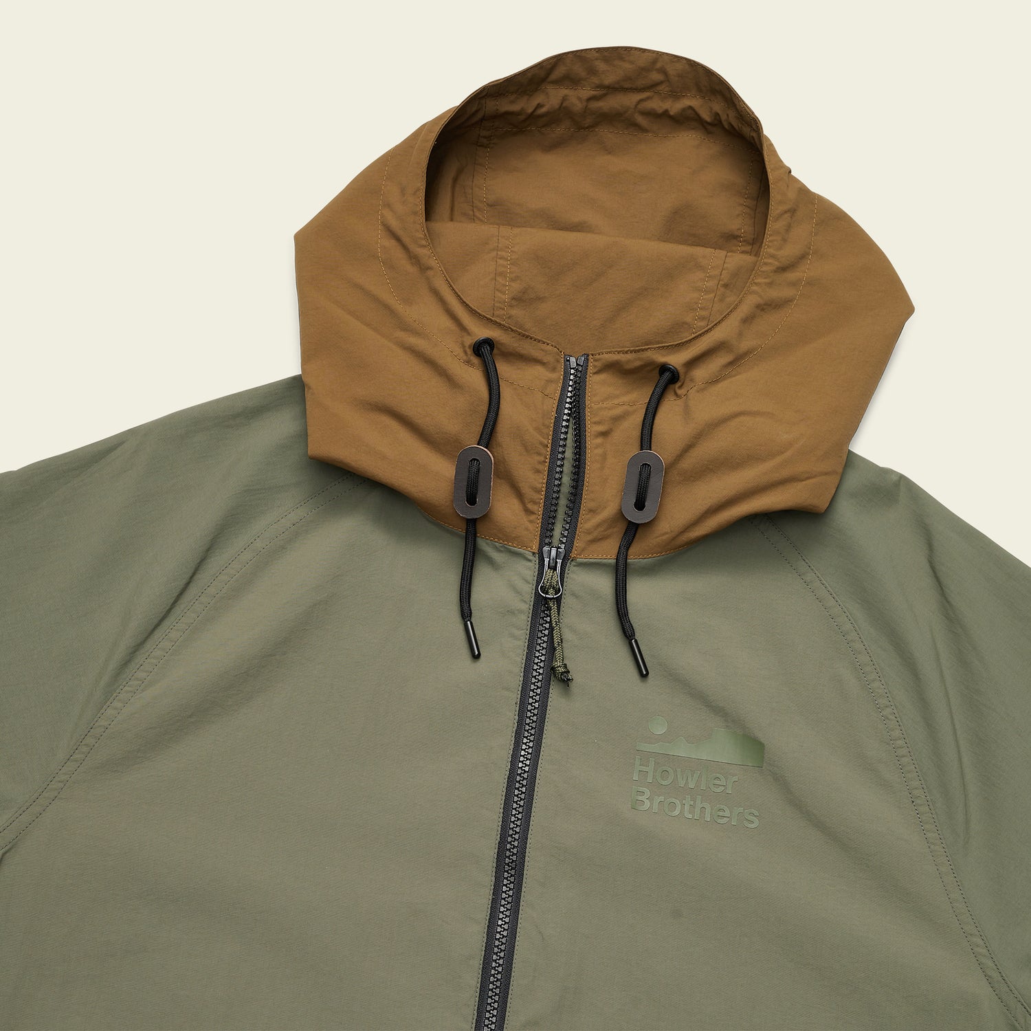 The Seabreacher Jacket is a lightweight windbreaker with an olive green body and brown hood, featuring a front zipper, black drawstrings with toggles, water resistant fabric, and a Howler Brothers logo on the chest. - View 7
