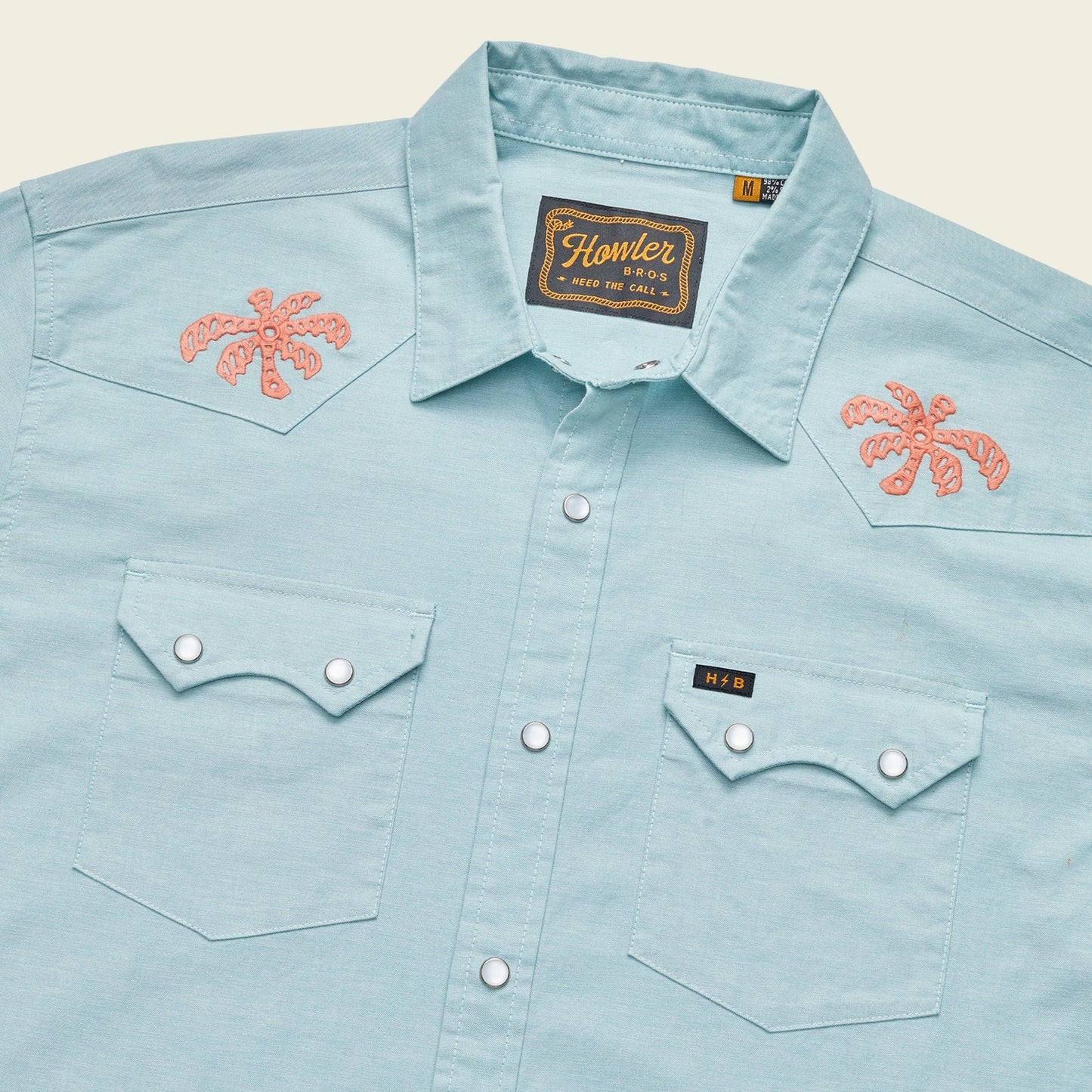 Light blue Crosscut Deluxe Shortsleeve western-style summer shirt with two front pockets, pearl snap buttons, and coral palm tree motif embroidery on the shoulders. A woven Howler brand label is visible inside the collar. - View 6