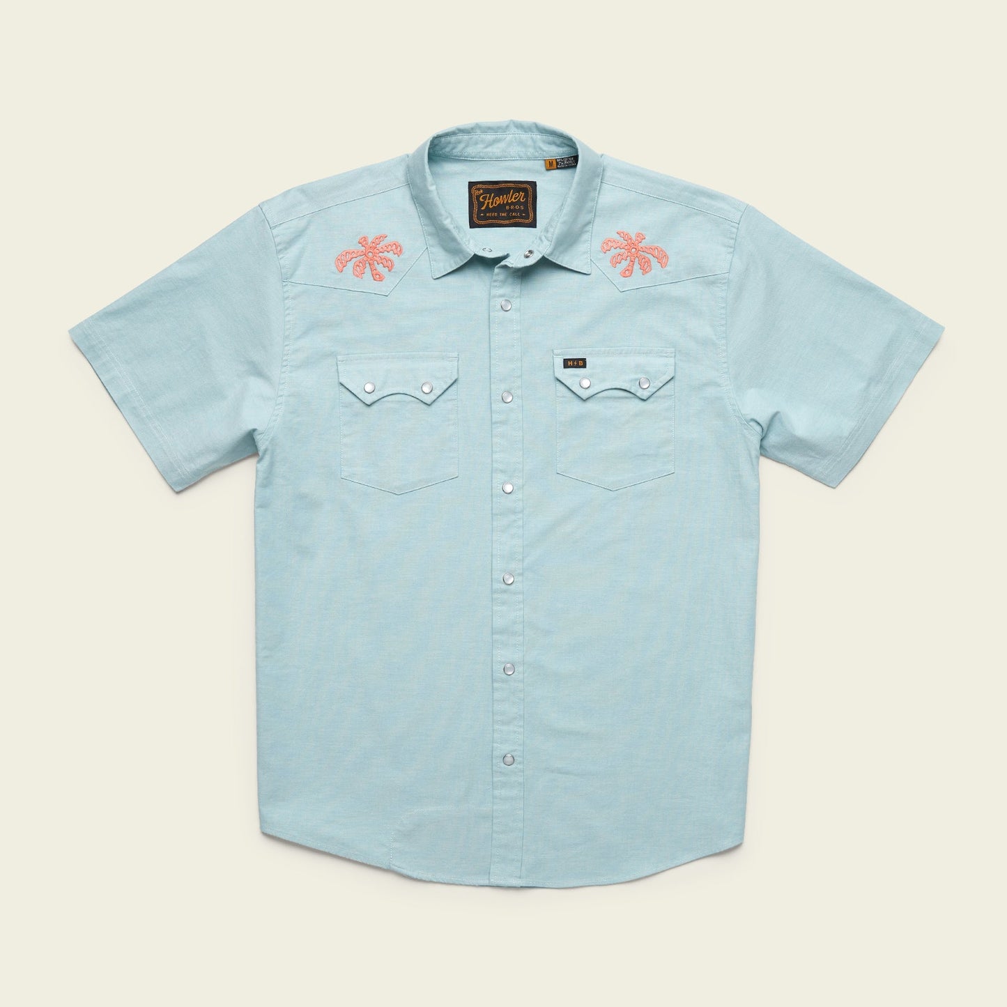 Light blue Crosscut Deluxe Shortsleeve summer shirt with two chest pockets; features pink motif embroidery of palm trees on both shoulders. Shirt is laid flat on a neutral background. - View 1
