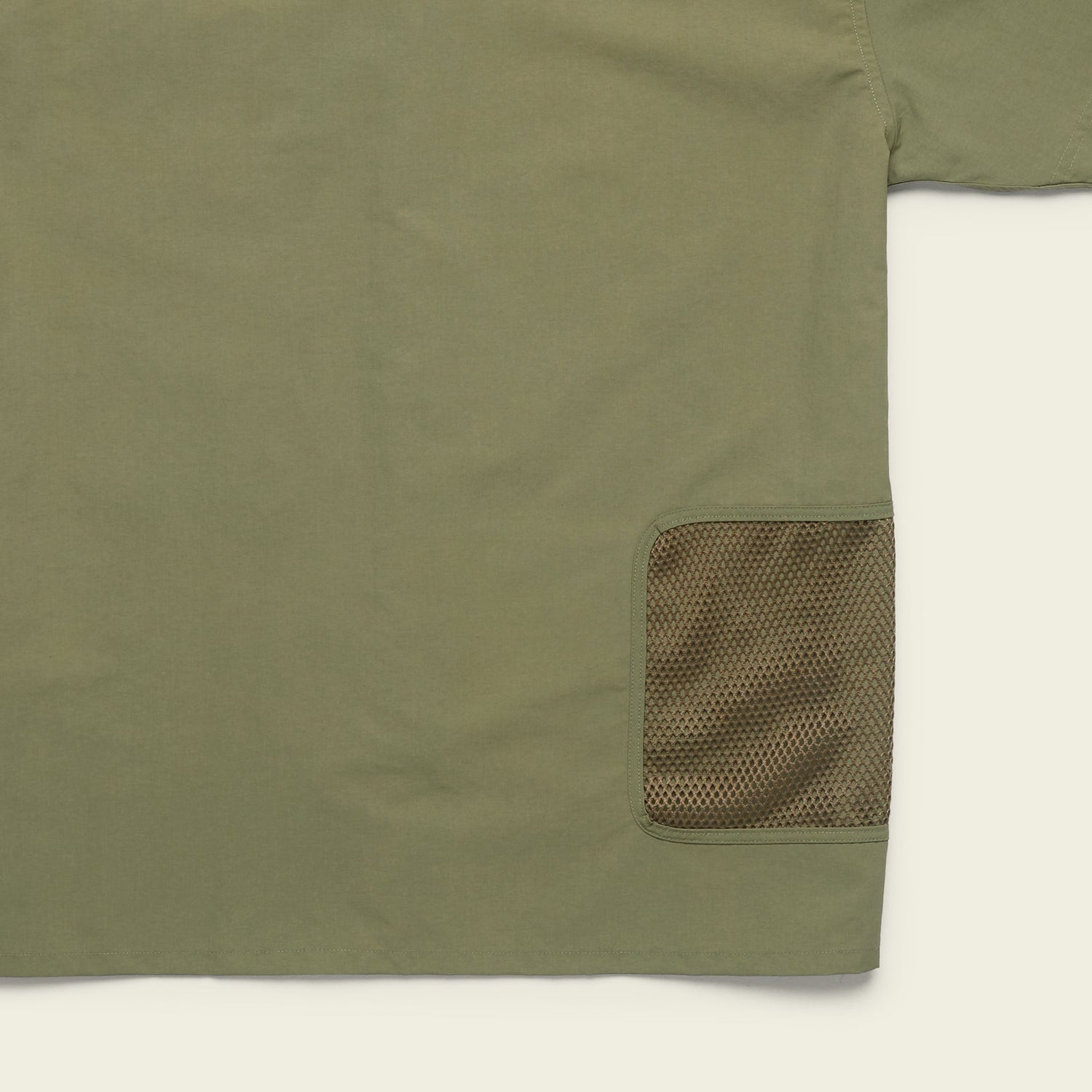 Olive green Forager Utility Shirt with a mesh brown pocket on the lower right side. Only part of this tech shirt is visible, focusing on pocket detail and fabric texture, perfect for hiking trails against a light background. - View 8
