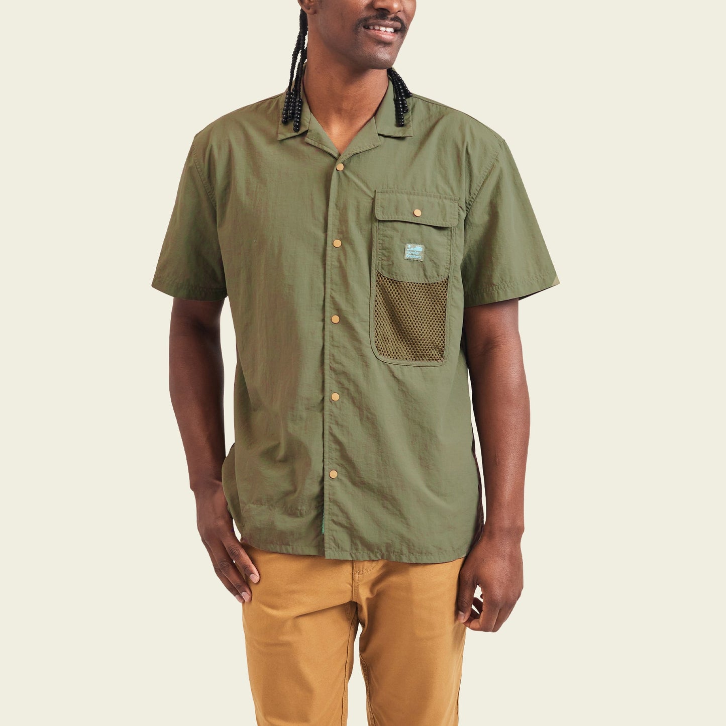 A person wearing a Forager Utility Shirt—an olive green, short-sleeve button-up with a mesh pocket—paired with tan pants, stands against a plain light background, ready for hiking trails. - View 4