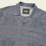 A blue short-sleeve Guayabera button-up shirt with two front pockets, unique embroidery, decorative stitching, and a Howler Bros label inside the collar.