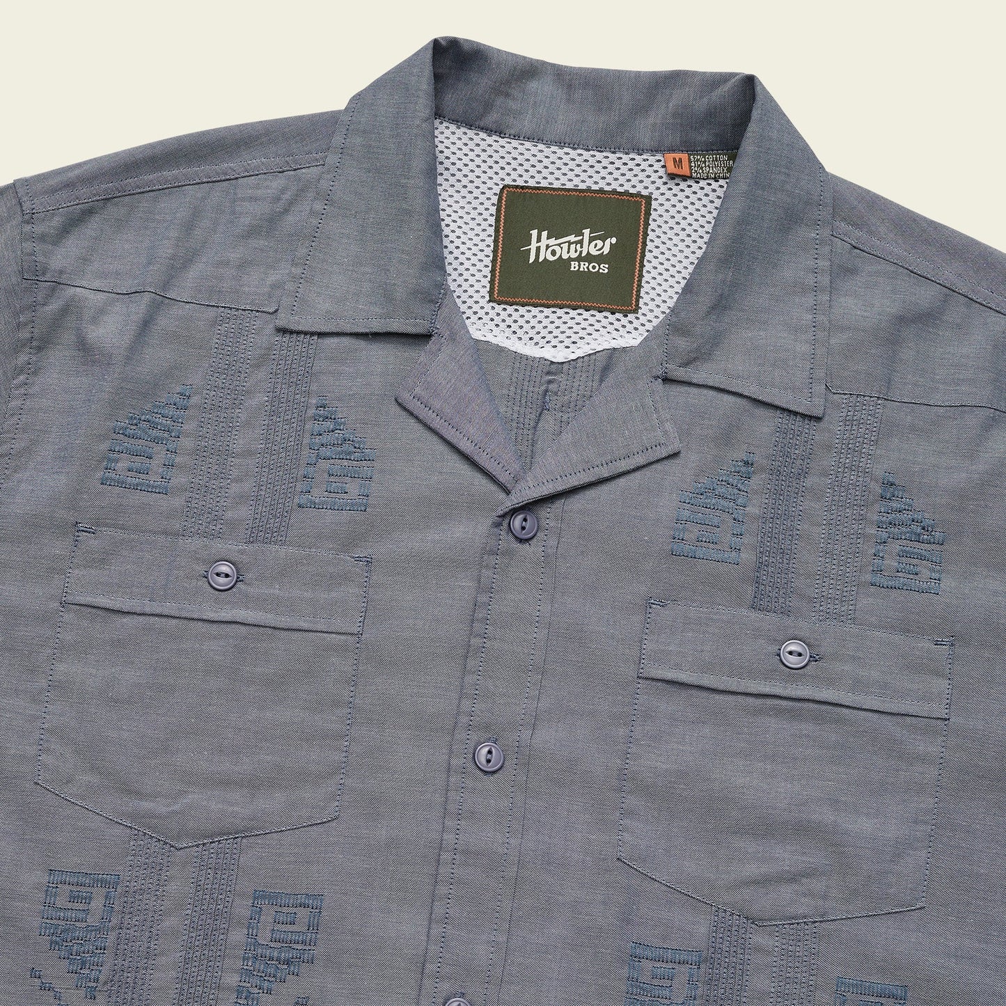 A blue short-sleeve Guayabera button-up shirt with two front pockets, unique embroidery, decorative stitching, and a Howler Bros label inside the collar. - View 6