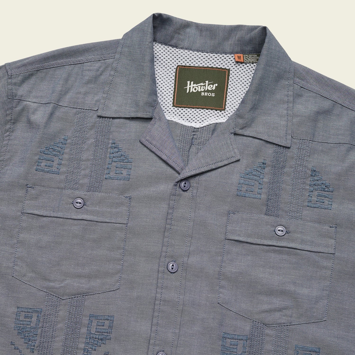 A blue short-sleeve Guayabera button-up shirt with two front pockets, unique embroidery, decorative stitching, and a Howler Bros label inside the collar. - View 6