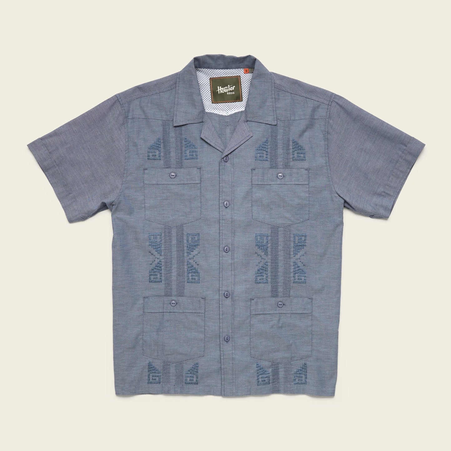 A short-sleeve, button-up blue Guayabera shirt with a subtle geometric pattern, two chest pockets, and unique embroidery, crafted from technical cotton-poly stretch fabric, displayed flat on a neutral background. - View 4