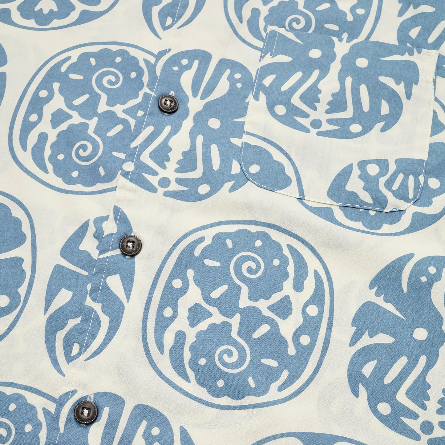 Close-up of a camp collar shirt featuring blue, abstract, circular patterns and black buttons. A chest pocket blending into the Sea Idols print is visible on the upper right, evoking classic vintage Hawaiian shirts. - View 3