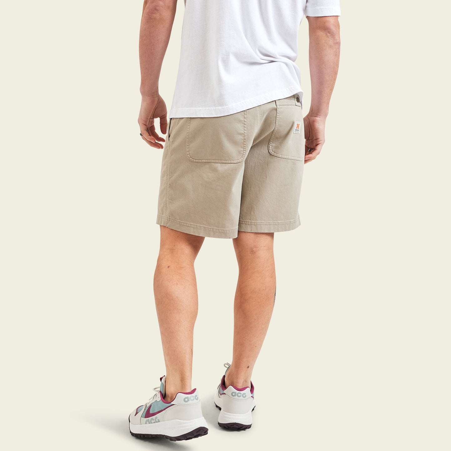 A person wearing a white t-shirt, cotton twill shorts with back pockets, and white sneakers with maroon and teal accents stands with their back facing the camera. - View 5