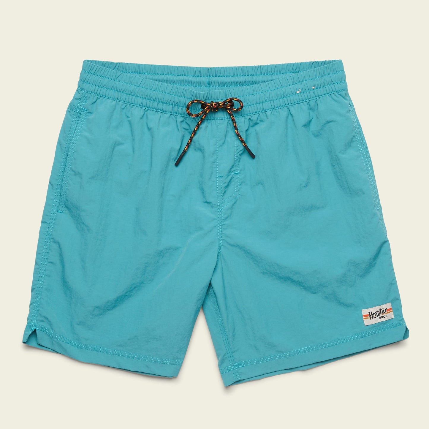 Bright turquoise quick drying nylon shorts with an elastic waistband, black and orange drawstring, side pockets, and a small rectangular brand patch on the lower left leg. The background is a pale beige color. - View 1