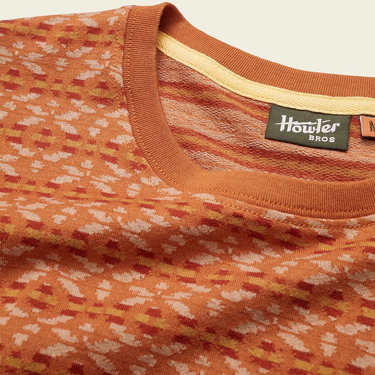 Close-up of an orange and beige patterned Howler Bros sweater, reminiscent of a vintage surf shirt, showing the collar, neck tag, and textured fabric details against a neutral background. - View 6