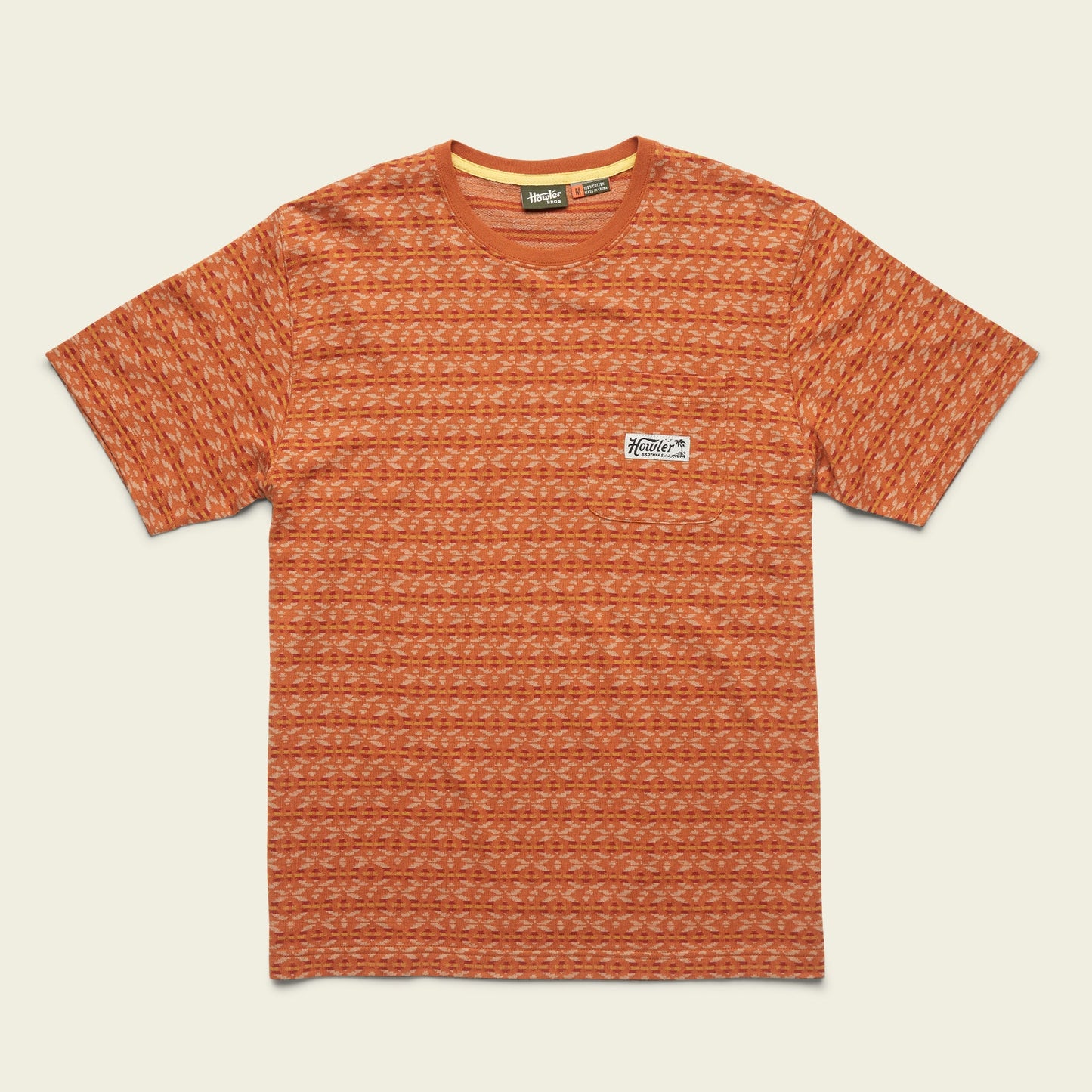 A short-sleeve orange patterned cotton jacquard t-shirt with a crew neckline and a small rectangular white patch featuring a logo on the left chest. The shirt is laid flat on a light background. - View 1
