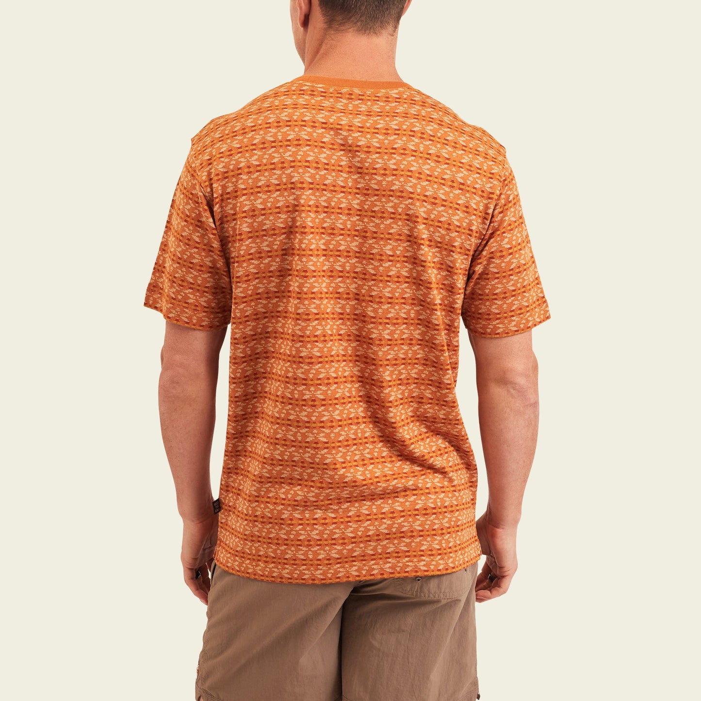 A man stands with his back to the camera, wearing a vintage surf shirt in orange patterns and light brown shorts against an off-white background. - View 5