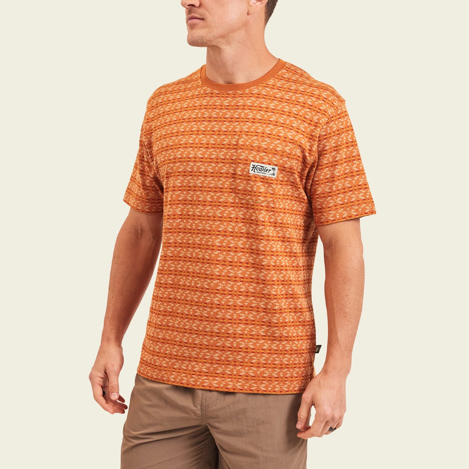 A man wearing a patterned orange vintage surf shirt with a small white patch on the chest, paired with light brown pants, standing against a plain light background. - View 4