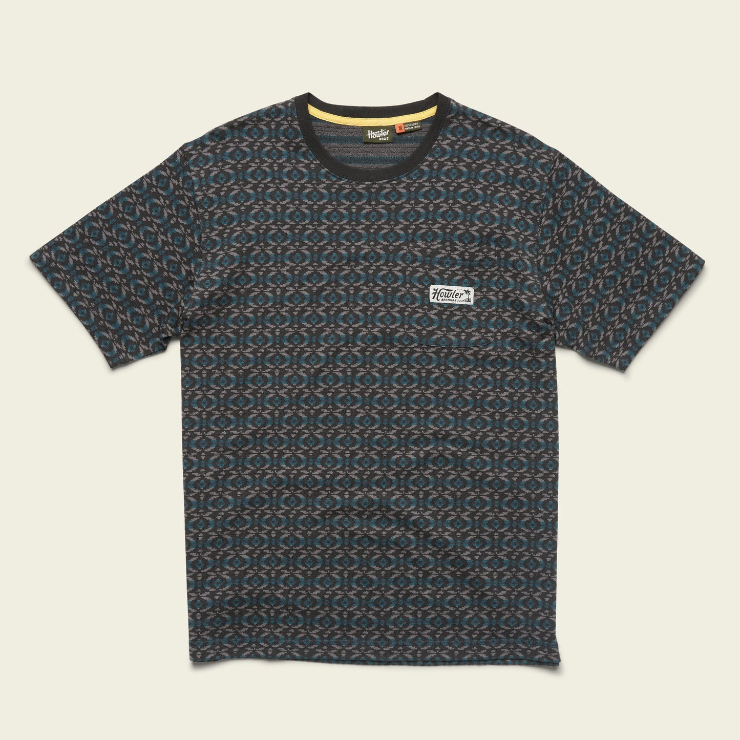 A short-sleeve, crew neck jacquard t-shirt featuring a blue and brown geometric pattern and a small white patch with text on the left chest. The 100% cotton shirt is laid flat on a light background. - View 2