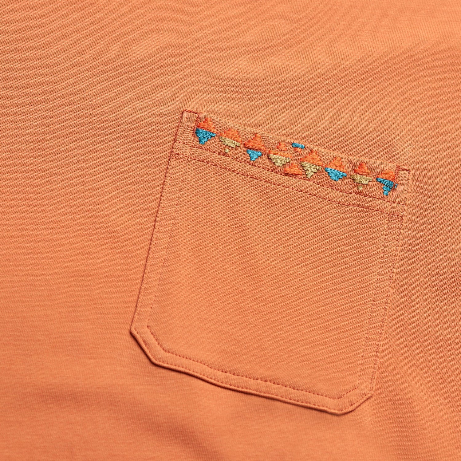 A close-up of an orange pocket t-shirt made from heavyweight cotton, featuring a row of small, colorful embroidered triangles along the top edge for an 80s 90s inspired touch. - View 3