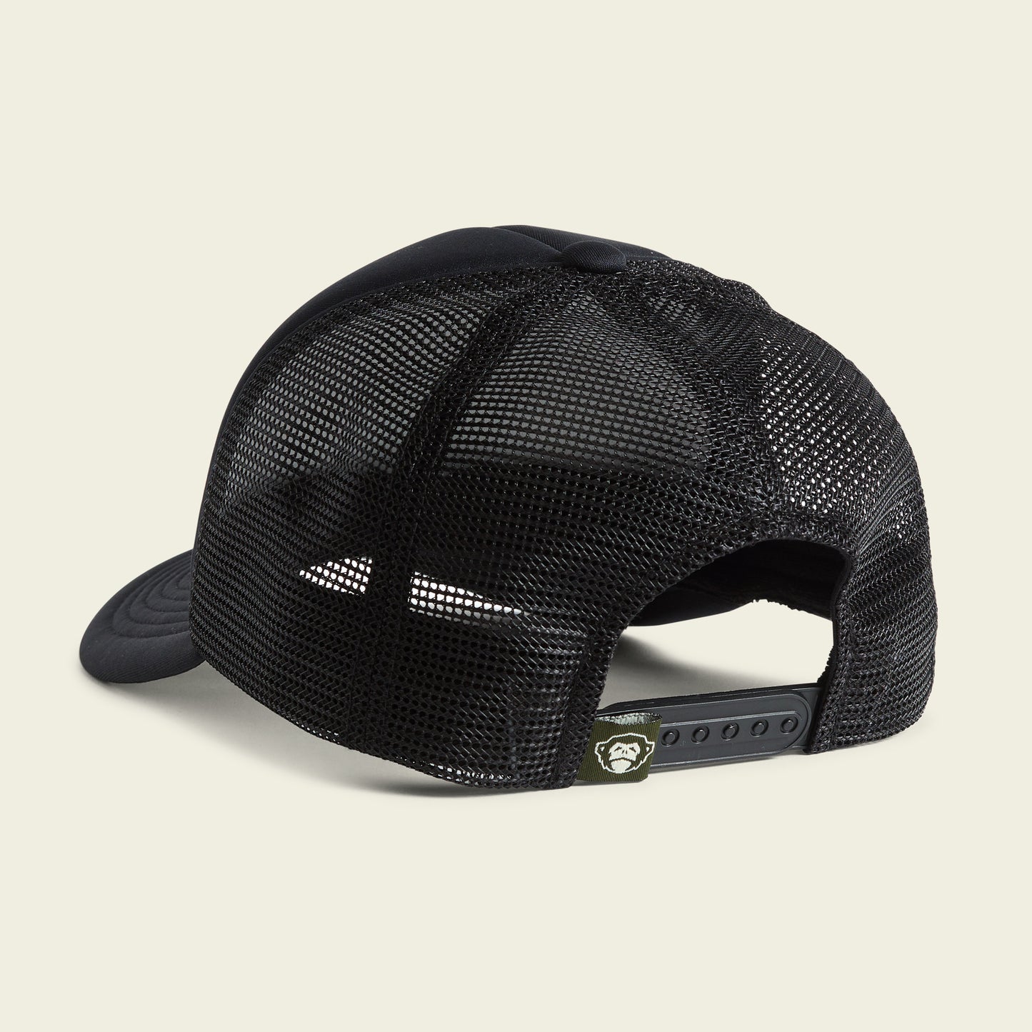 A black mesh trucker cap shown from the back, featuring a snapback closure and a small green tag with a white graphic on the adjustable strap, this vintage-inspired hat offers classic style and comfort. - View 3