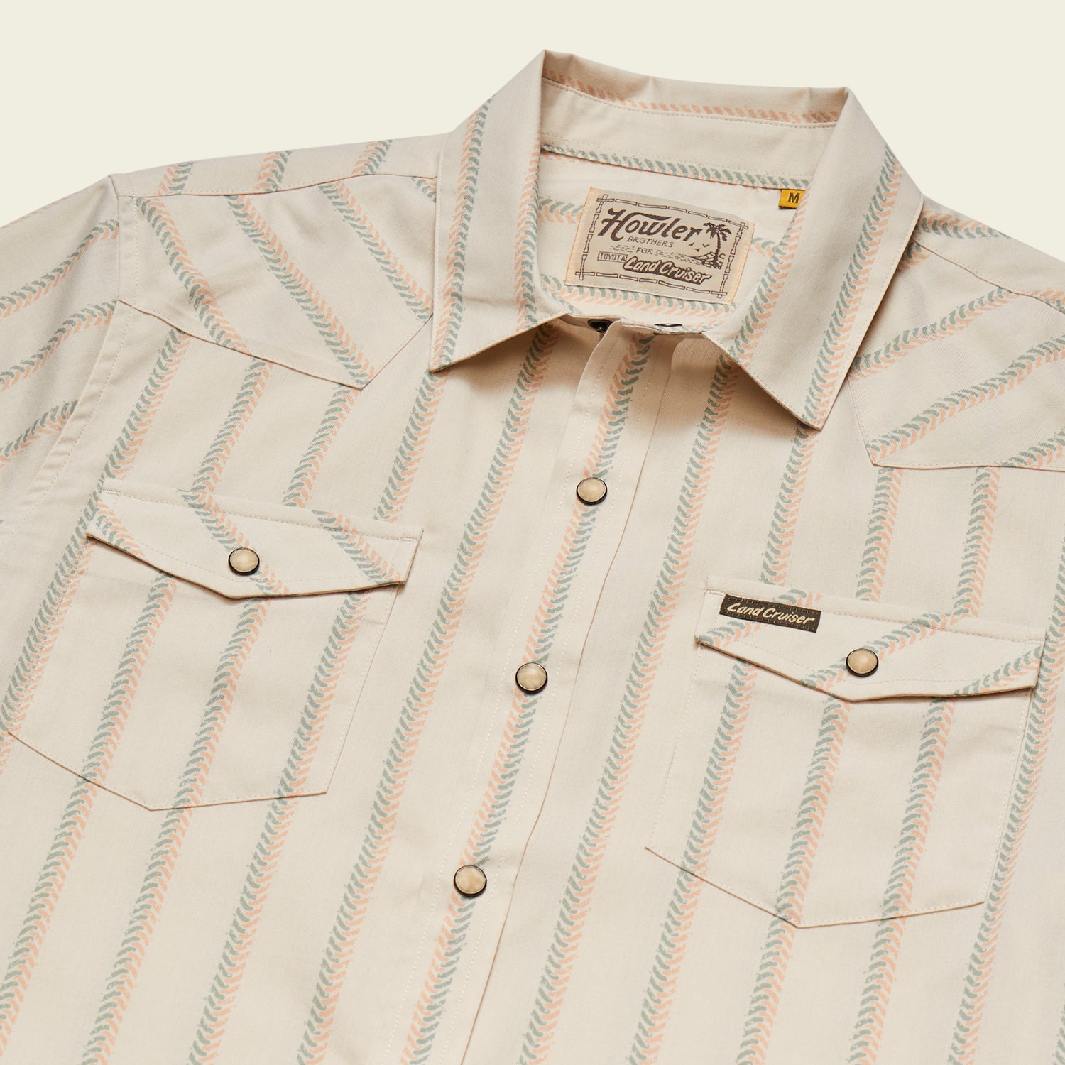A vintage inspired shirt from Howler Brothers, this beige short-sleeve button-up features light blue and orange diagonal stripes, two front flap pockets, brown snap buttons, and a “Howler” label above the left pocket. - View 3