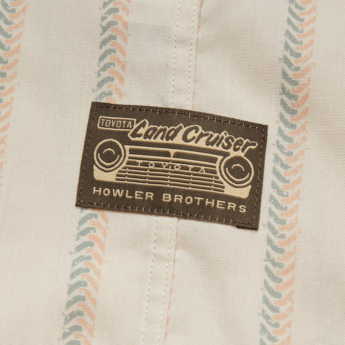 A fabric patch featuring a vintage Toyota Land Cruiser grille design and the text “Toyota Land Cruiser” and “Howler Brothers,” sewn onto a beige cloth with a pastel striped pattern, perfect for fans of vintage inspired shirts. - View 4