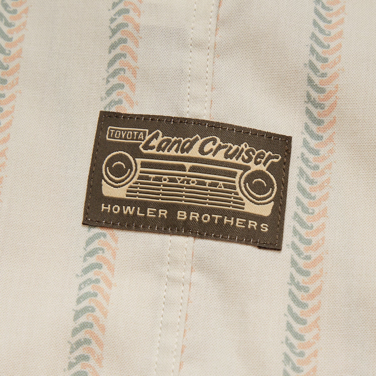 A fabric patch featuring a vintage Toyota Land Cruiser grille design and the text “Toyota Land Cruiser” and “Howler Brothers,” sewn onto a beige cloth with a pastel striped pattern, perfect for fans of vintage inspired shirts. - View 4