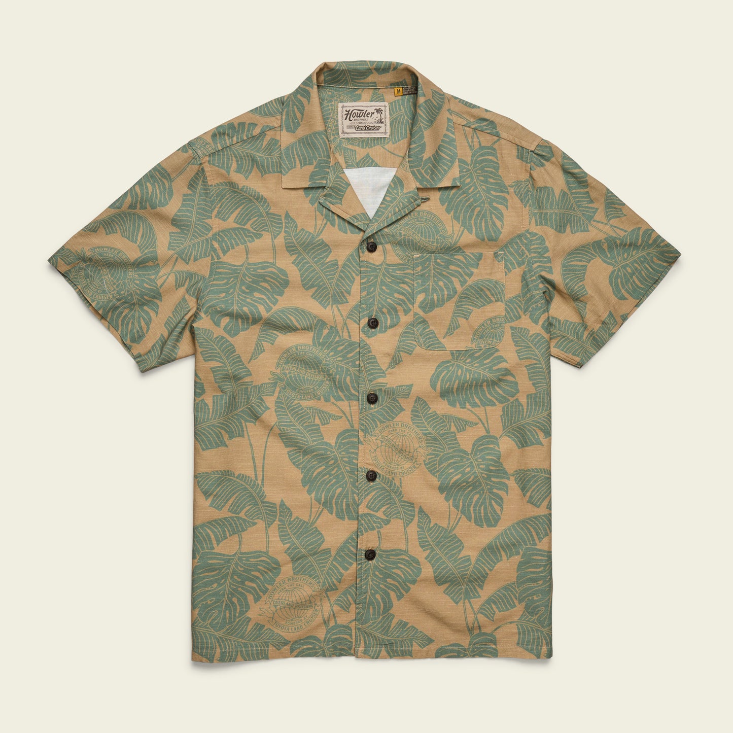 A short-sleeve, button-up Monoloha Shirt with a beige background and green leaf pattern, featuring a collar and front pocket. Inspired by vintage Hawaiian shirts, it offers a casual, tropical style perfect for any getaway. - View 1