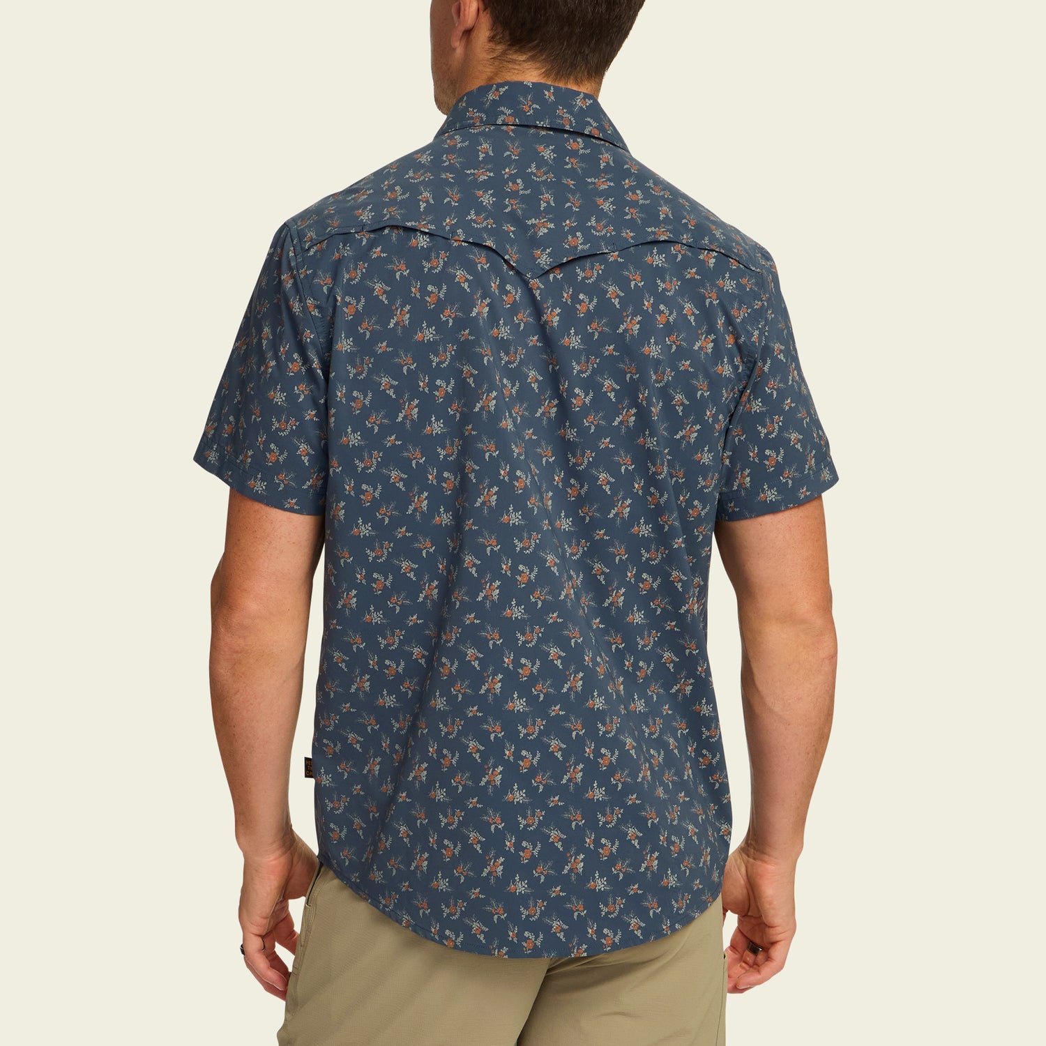 A man is standing with his back to the camera, wearing a blue technical utility shirt with a small floral pattern and beige shorts. The short-sleeve shirt features a vented rear yoke for added comfort. - View 5