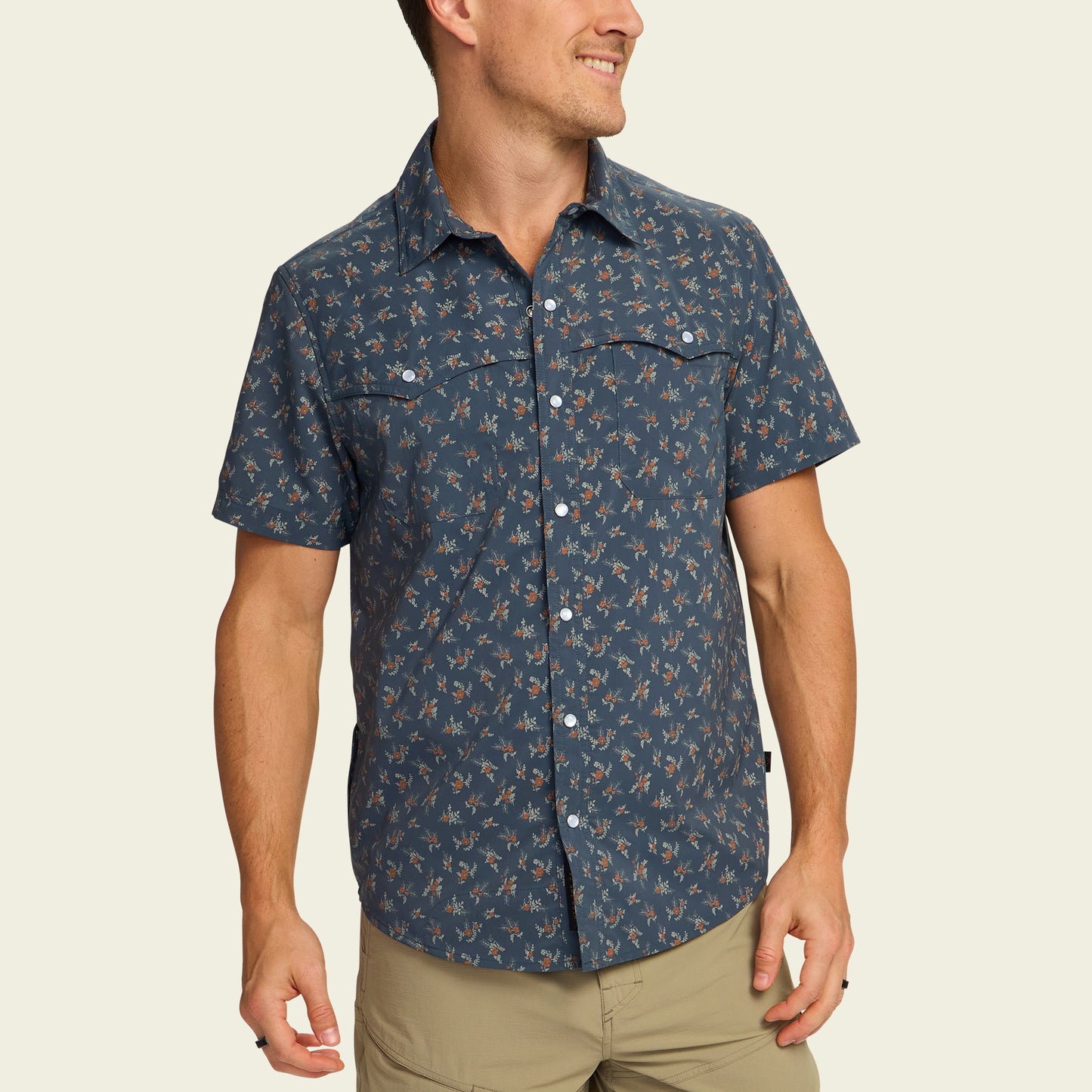 A man wearing a pearl snap, short-sleeve blue shirt with a small floral pattern and beige pants, smiling and looking to his left. - View 4