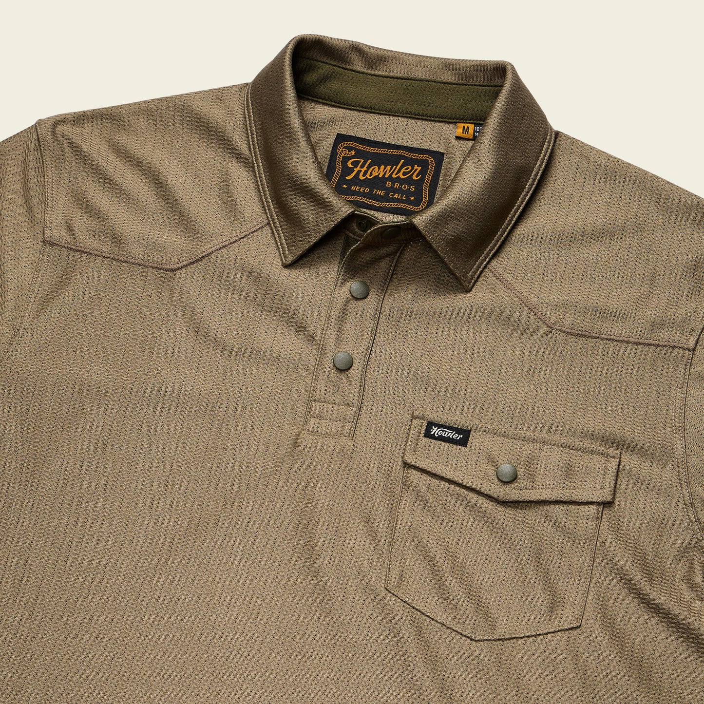 A khaki-colored tech polo with a button-up placket and buttoned chest pocket. Made from recycled polyester, it features a subtle textured pattern, Howler Bros. label inside the collar, and a small Howler tag on the pocket. - View 3