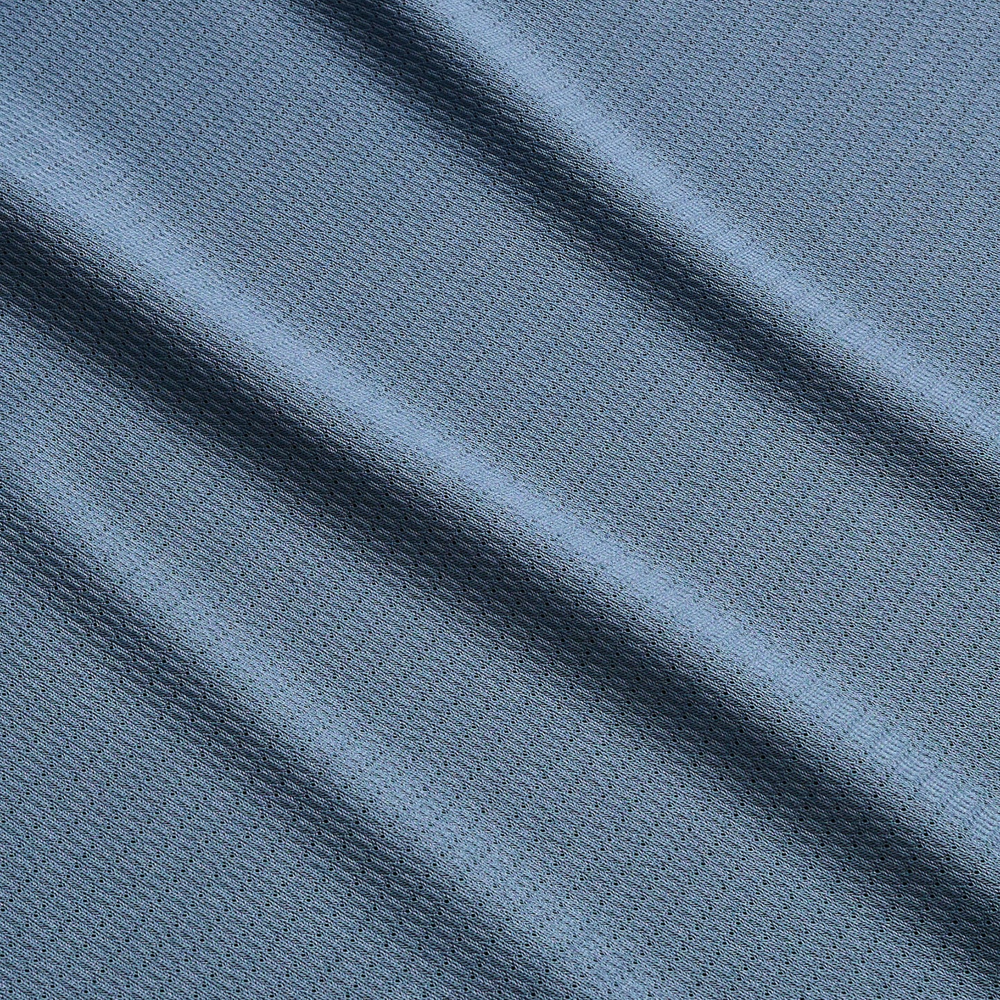 Close-up of textured blue Tech Polo fabric with small geometric patterns, featuring soft diagonal folds that create gentle shadows and highlights across the surface. Crafted from breathable recycled polyester for quick drying comfort. - View 4