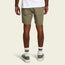 A person stands facing away, wearing Quonset Camp Shorts in olive green ripstop cotton, a white T-shirt, white socks with blue and red stripes, and green sneakers, set against a plain light background.