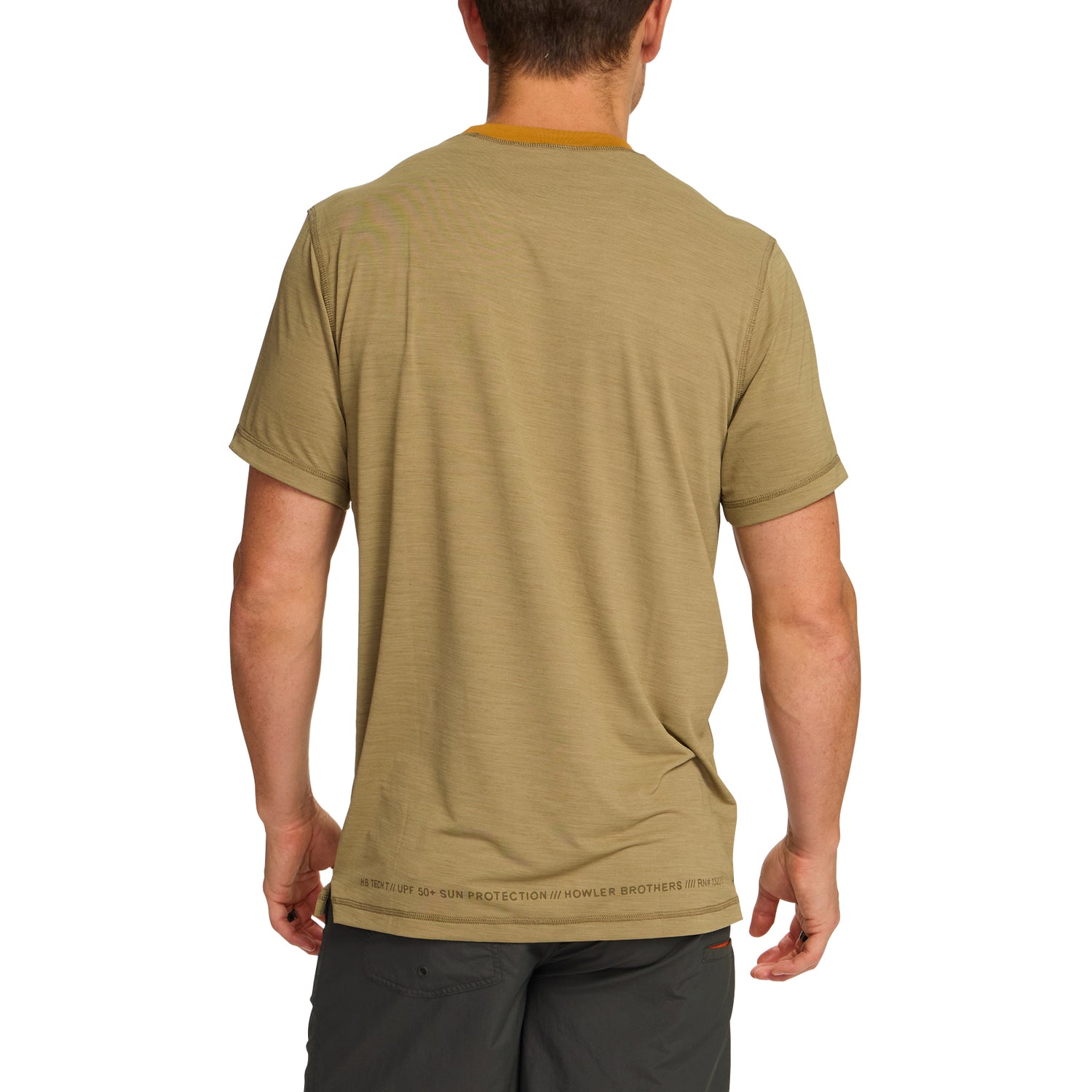 A man stands with his back to the camera, wearing a light brown shortsleeve tech shirt made from a polyester spandex blend and dark gray shorts. Subtle text lines the bottom hem of the shirt. The background is plain white. - View 4