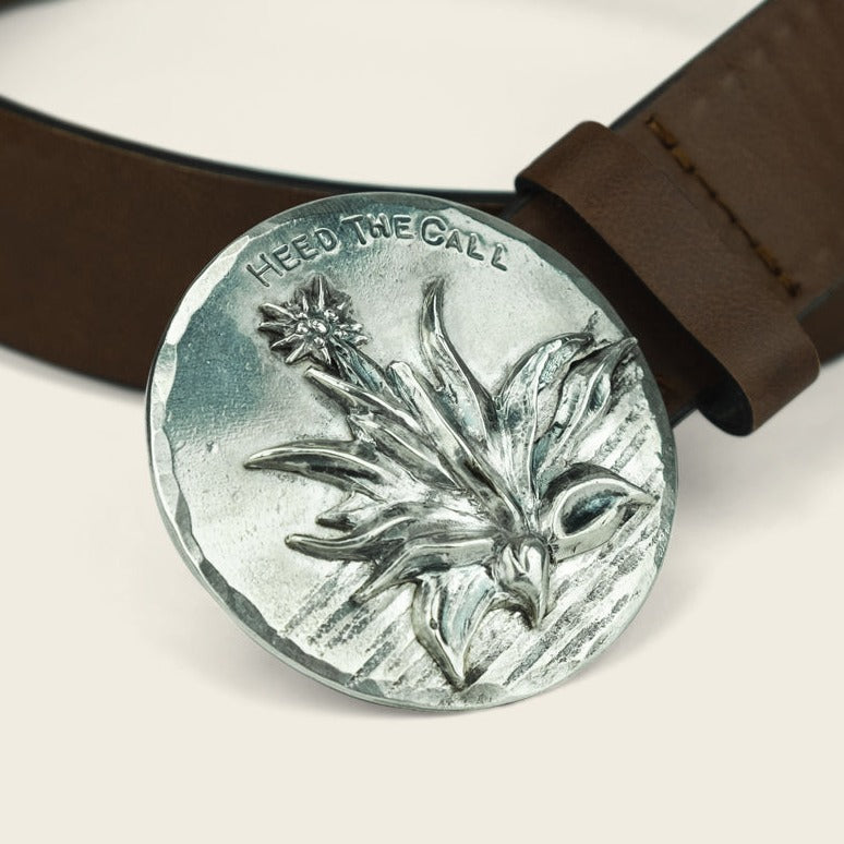 A Cityboy Forge silver belt buckle with a raised flower design and the phrase HEED THE CALL engraved above it, attached to a brown leather belt—perfect for fans of Howler Brothers style. - View 2