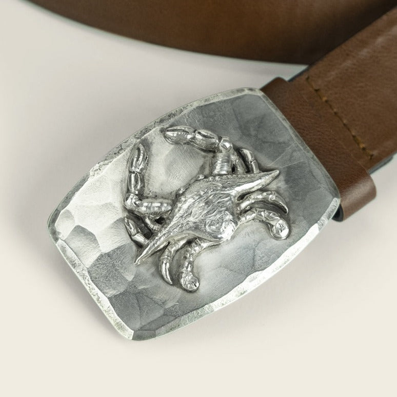 A brown leather belt with a sterling silver buckle by Cityboy Forge, featuring a detailed 3D crab design on a hammered metal background.