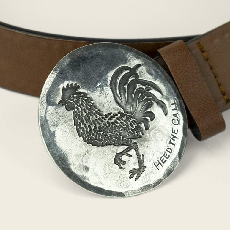 A round, silver El Gallo buckle from Cityboy Forge, embossed with a rooster and the words “HEED THE CALL,” attached to a brown leather belt. - View 2
