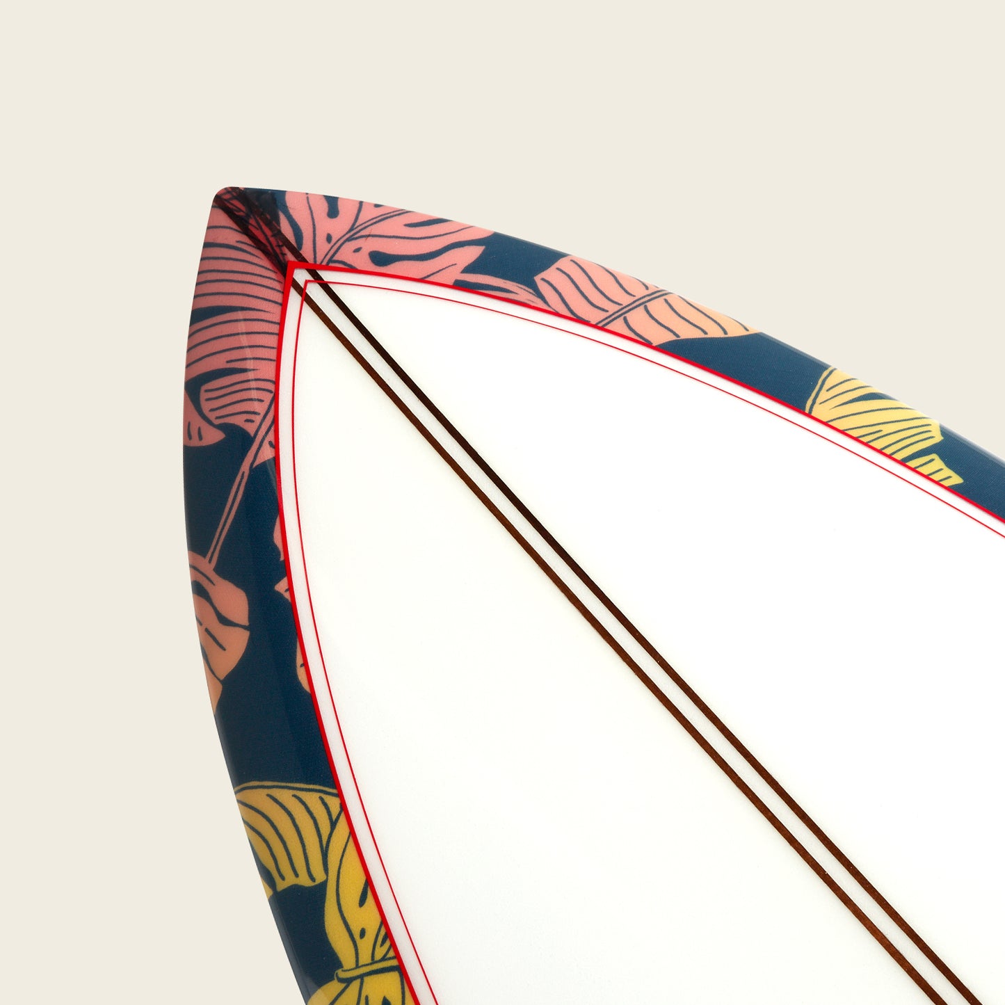 Close-up of the tip of an Almond Surfboards surfboard with a white center, red outline, and a dark blue border featuring a colorful tropical leaf pattern in pink and yellow. The background is a plain off-white. - View 3